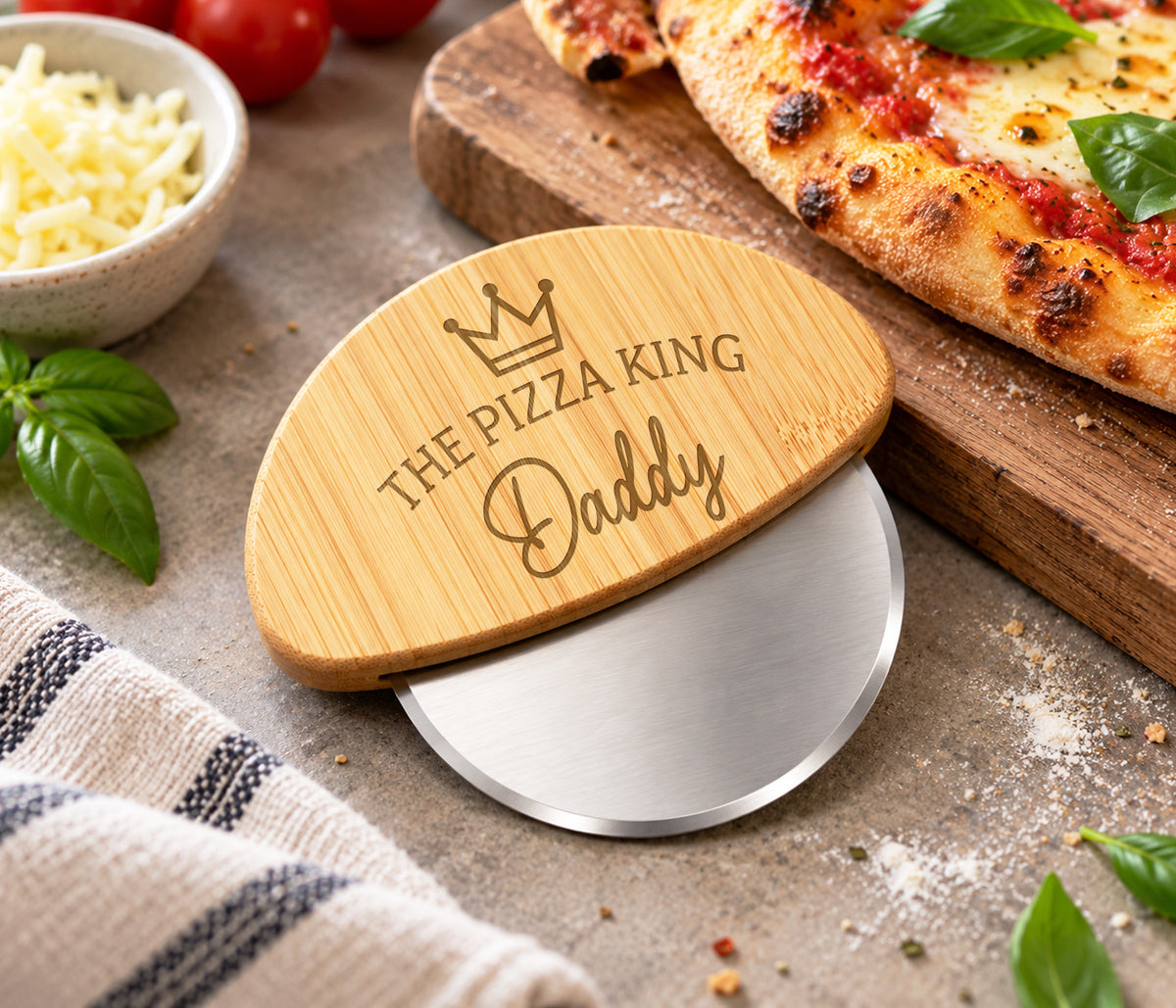 A personalized pizza cutter with a bamboo handle engraved with 'THE PIZZA KING Daddy' and a crown, There is a stainless steel wheel to cut the pizza.