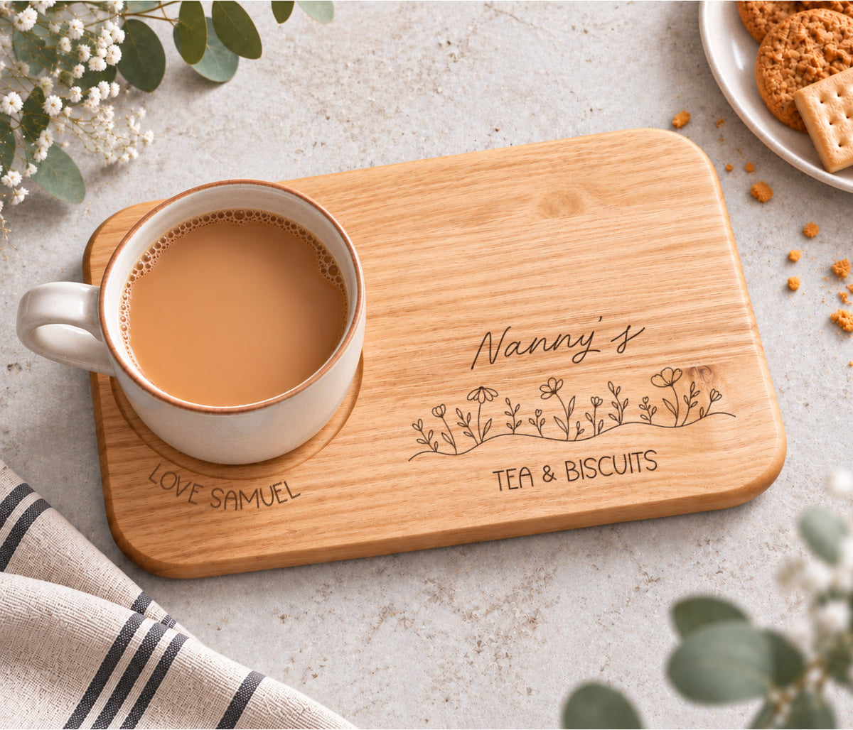 A rectangular wooden serving tray engraved with 'Nanny's TEA & BISCUITS' and a line of wildflowers, with love and the child / childrens name wrapped around the mug indent.
