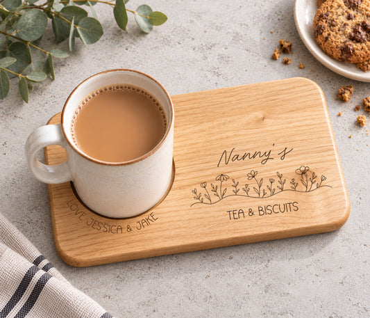 A rectangular wooden serving tray engraved with 'Nanny's TEA & BISCUITS' and a line of wildflowers, with love and the child / childrens name wrapped around the mug indent.