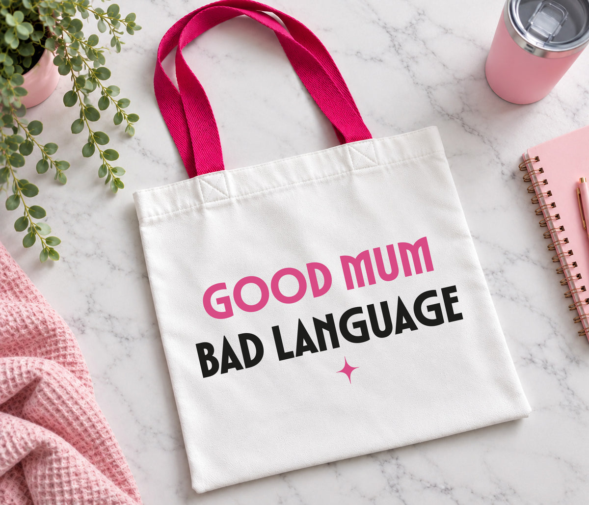 White tote bag with bright pink handles and the wording good mum bad language. in bold black and pink lettering.
