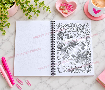 An open spiral-bound notebook on a marble surface, featuring a school-themed maze and the text 'HELP ME ESCAPE THIS shithole!' on one page. The notebook is surrounded by pink stationery, a plant, a coffee cup, and binder clips.