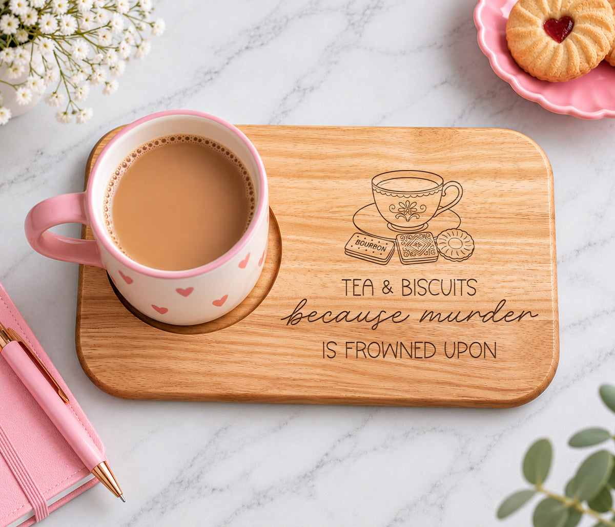 A rectangular wooden tray with rounded corners sits on a white marble surface. The tray is engraved with a teacup, biscuits, and the phrase 'TEA & BISCUITS because murder IS FROWNED UPON.