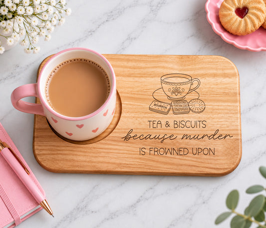 A rectangular wooden tray with rounded corners sits on a white marble surface. The tray is engraved with a teacup, biscuits, and the phrase 'TEA & BISCUITS because murder IS FROWNED UPON.